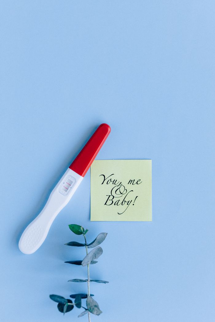 Minimalist flat lay of a positive pregnancy test with a note on a pastel blue background.